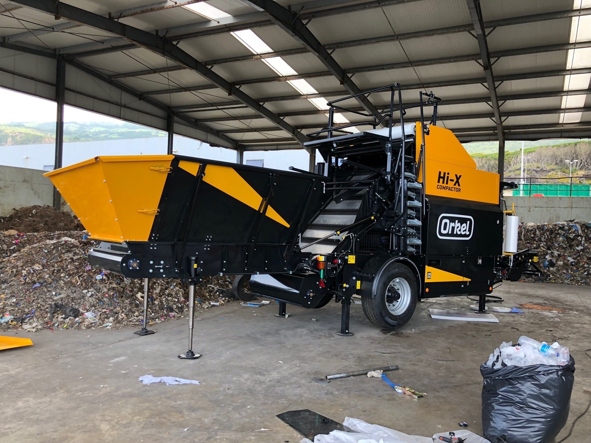A Hi-X compactor inside a concrete facility with landfill waste piled in the background.
