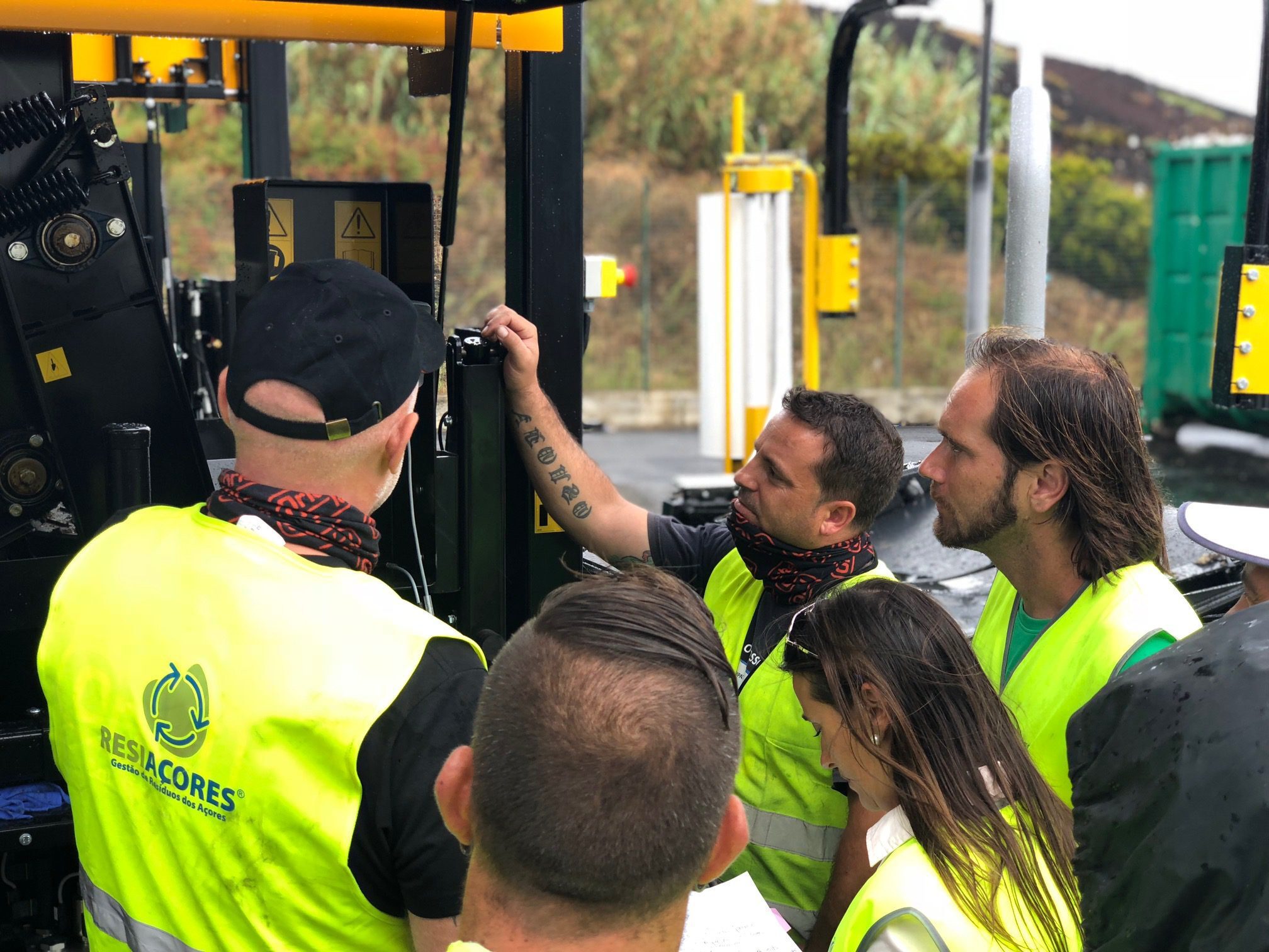 Technicians wearing yellow safety vests gathered in front of a black and yellow machine.