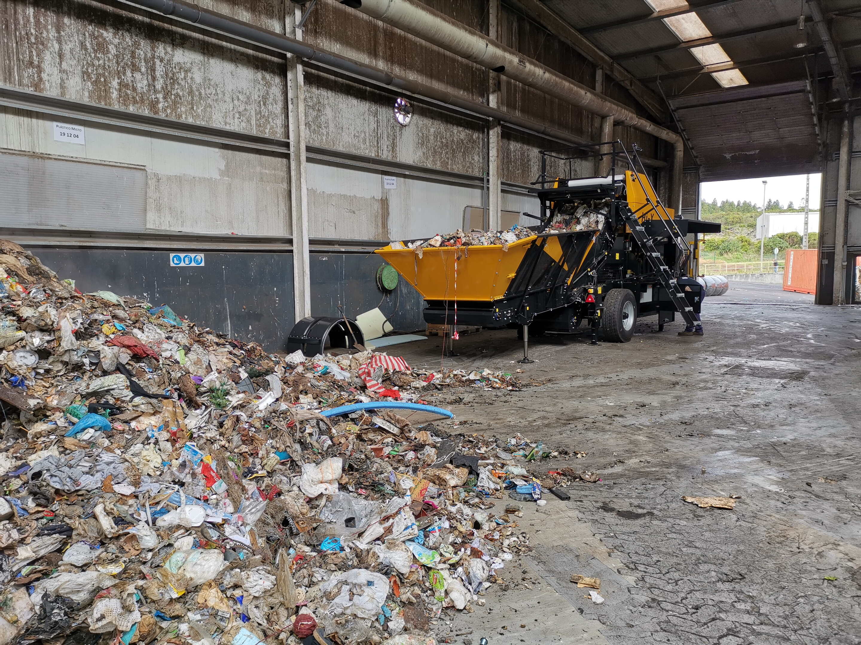 A Hi-X compactor in a concrete facility, with loose landfill waste in its feeding table and heaps of loose waste in the foreground.